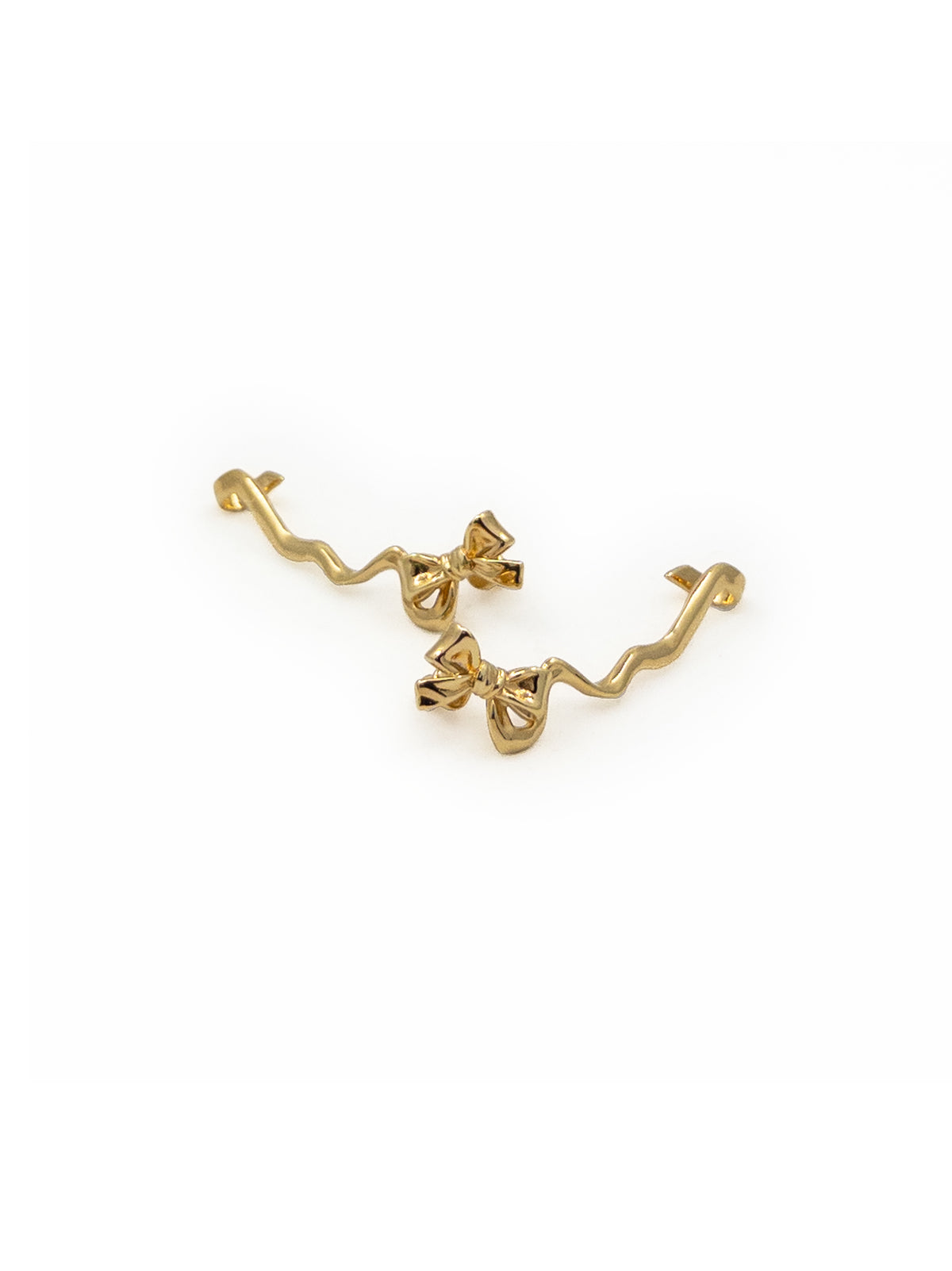 A pair of gold-toned ear cuffs with wavy outer bands and small bow details, displayed on a clean white background.